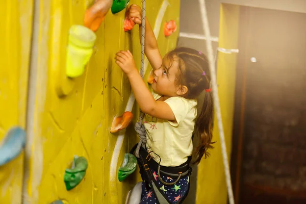 little girl climbing a rock wall indoor