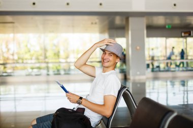 Mutlu adam havaalanında, bekleme odasında oturup şapka tutar pasaport ve bilet