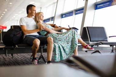 Havaalanında bekleme odası, sandalye üzerinde oturan genç bir çift. Uzun uçak bekliyor