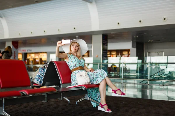 Τουριστική Ξανθιά Κοπέλα Καπέλο Που Κάθεται Ένα Αεροδρόμιο Και Κάνει — Φωτογραφία Αρχείου