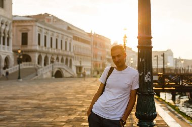 Genç yakışıklı adam Venedik'te San Marco meydanında şafakta, İtalya, ayakta beyaz t-shirt giyen