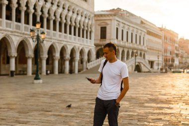 Beyaz t-shirt giyen telefon Venedik'te San Marco meydanında şafakta, İtalya, izleyen genç yakışıklı adamım