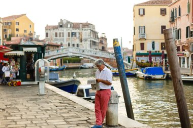 Venice, İtalya - 21 Temmuz 2017: Venedik bir kanalınkıyısında otururken bir gazete okuyan adam.