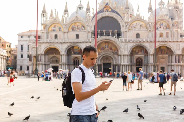 Young Handsome man watching at phone in San Marco Square in Venice at dawn, Italy