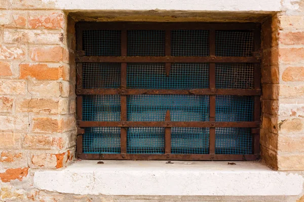 Fragment of old abandoned brick house with closed window behind iron bars in small italian town , Italy.