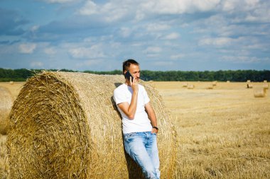 Mutlu gülümseyen adam akıllı telefon ayakta saman yığını yakınındaki buğday alanı kullanma 