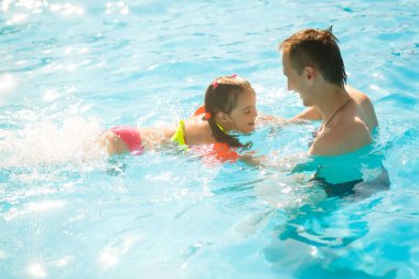 Tropikal tatil Havuzda yüzmek için yürümeye başlayan çocuk kızı öğretim etkin baba. Yaz tatillerini ve spor kavram