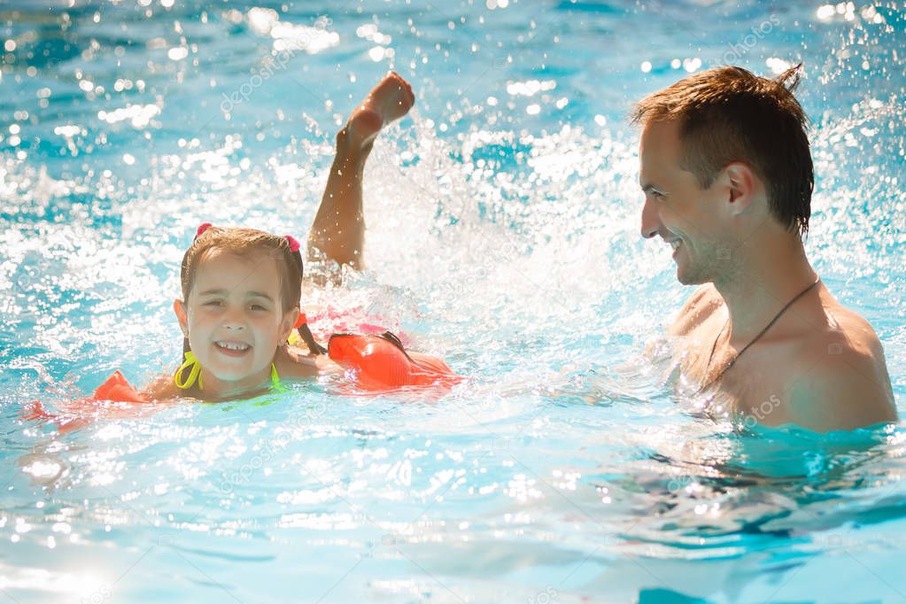 Active father teaching his little daughter to swim in pool on tropical resort. Summer vacations and sport concept