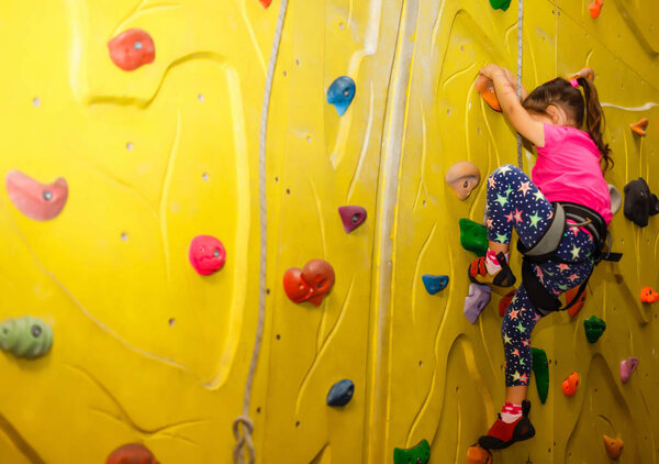 little girl in a pink T-shirt climbing a rock wall indoor