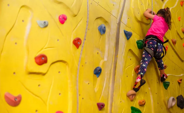 little girl in a pink T-shirt climbing a rock wall indoor