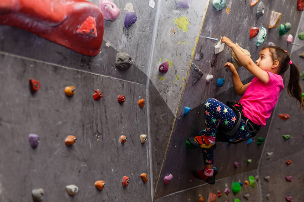little girl in a pink T-shirt climbing a rock wall indoor