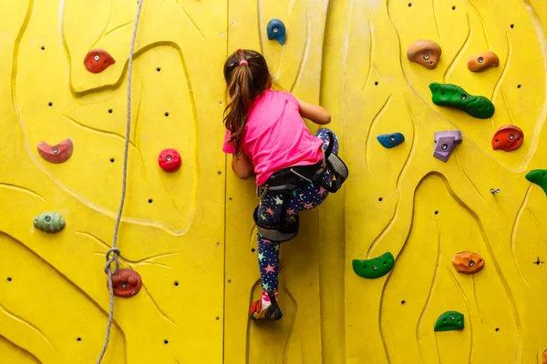 little girl in a pink T-shirt climbing a rock wall indoor