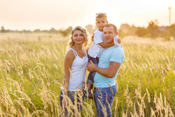 年轻的家庭与儿子散步和有良好的时间在绿色田野在日落 — 图库照片