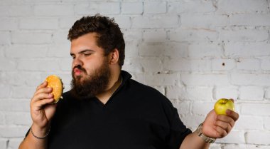 Açgözlülükle hamburger yeme ve yeşil elma beyaz zemin üzerine başka bir elinde tutan sakallı adam heyecanlı