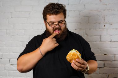 Şişman adam iştahla yemek Hamburger beyaz tuğla duvar arka plan üzerinde