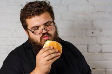 Şişman adam iştahla yemek Hamburger beyaz tuğla duvar arka plan üzerinde