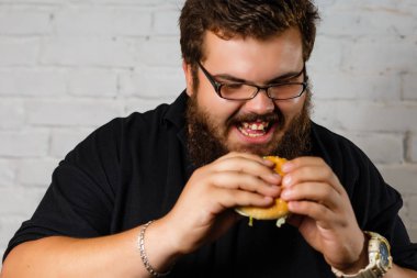Şişman adam iştahla yemek Hamburger beyaz tuğla duvar arka plan üzerinde