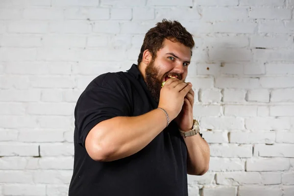 Hombre Gordo Comiendo Hamburguesa Codiciosamente Sobre Fondo Pared Ladrillo Blanco — Foto de Stock