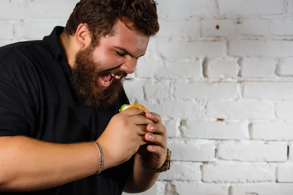 脂肪男欲張って食べるハンバーガー白いレンガ壁の背景に — ストック写真