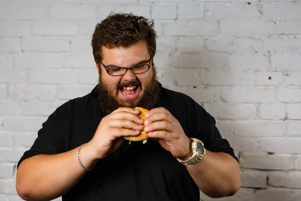 Hombre Gordo Comiendo Hamburguesa Codiciosamente Sobre Fondo Pared Ladrillo Blanco — Foto de Stock