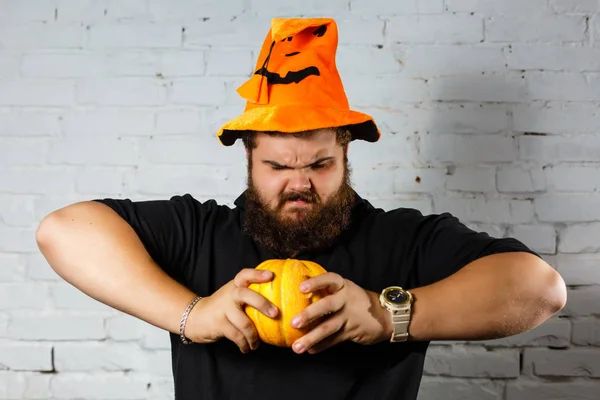 Halloween hipster with beard smiling in wizard hat. Man with pumpkin on white brick wall. Trick or treat. Holiday celebration concept.