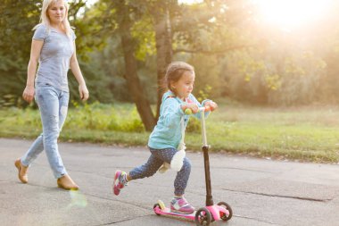 Genç Anne küçük kızı Park scooter binmek için öğretim