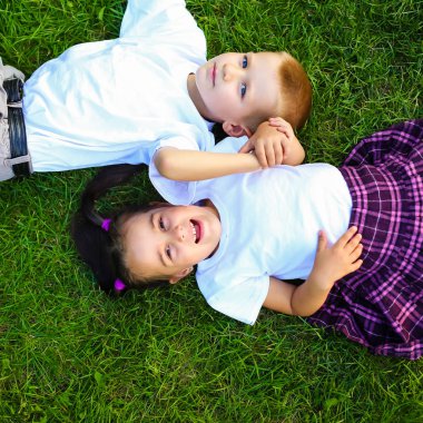 yaz zaman zevk. Ellerini başının arkasında tutarak ve birlikte yeşil çimenlerin üzerinde yatarken bir gülümseme ile birbirine bakarak iki sevimli küçük çocuk Üstten Görünüm