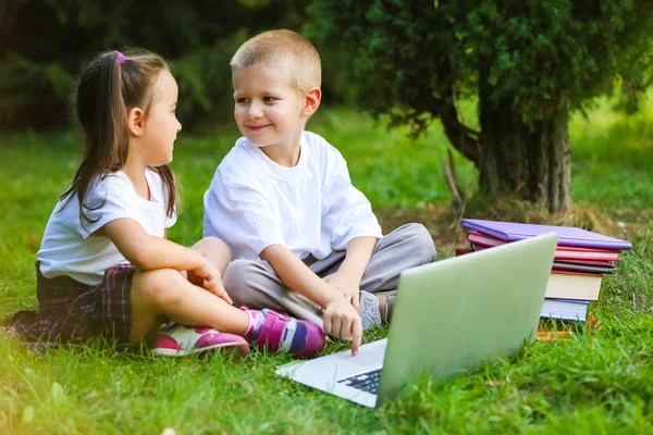 schoolboy and girl in park watching laptop