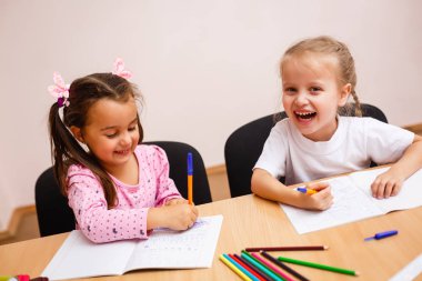 Sevimli küçük kız okulda masada oturan pesn kullanarak yazma
