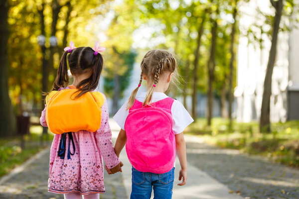 Two beautiful girlfriends girls going to school holding hands. Back to school