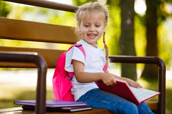 Kleines Schulmädchen Mit Rucksack Sitzt Auf Einer Bank Mit Einem — Stockfoto