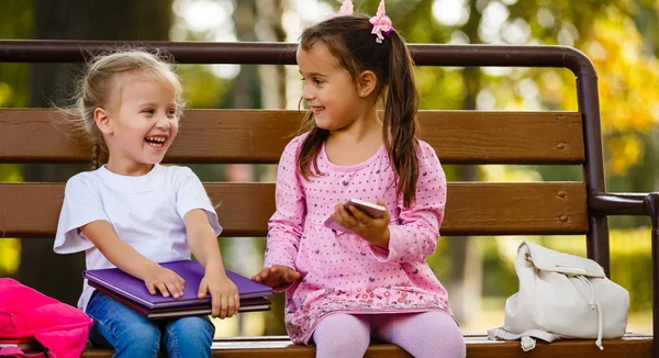 两个女孩坐在公园长凳上的书 — 图库照片