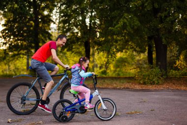 mutlu genç baba ve küçük kızı Bisiklet yeşil park, yan görünüm