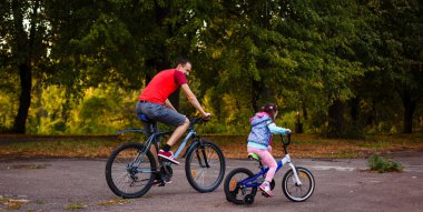 mutlu genç baba ve küçük kızı Bisiklet yeşil park, yan görünüm