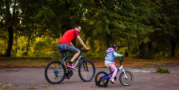 mutlu genç baba ve küçük kızı Bisiklet yeşil park, yan görünüm