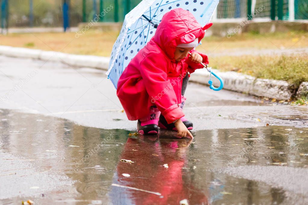 Adorable little girl with colorful umbrella playing in puddle outdoors at autumn rainy day 