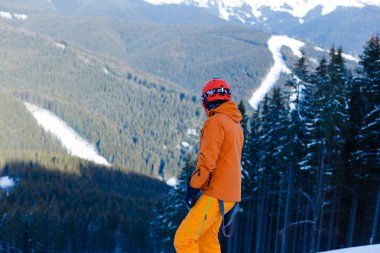 Turuncu kayak kıyafeti giymiş mutlu adam beyaz kar üzerinde dinleniyor