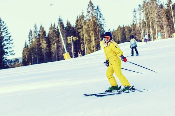 雪山でスキーに乗って黄色冬ジャンプ スーツの女性 — ストック写真