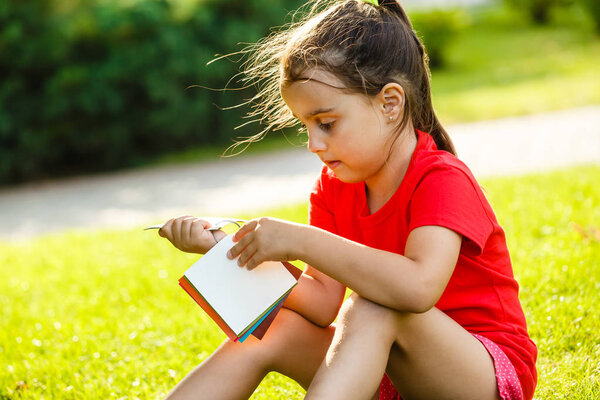 Little brunette girl choosing color of paint on color palette in sunny park