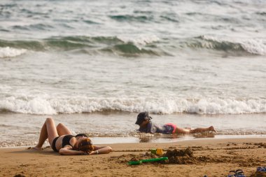 Genç bir kadın sahilde oturuyor ve sörf tahtasıyla oynuyor.
