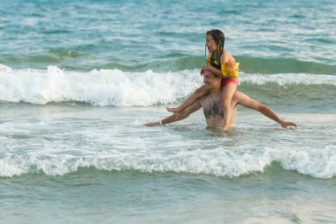 Genç baba ve kızı okyanus suyunda eğleniyor. 