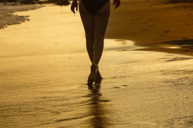 Gün batımında kumlu plajda okyanus dalgaları üzerinde yürüyen bacaklar siluetinin yakın görünümü