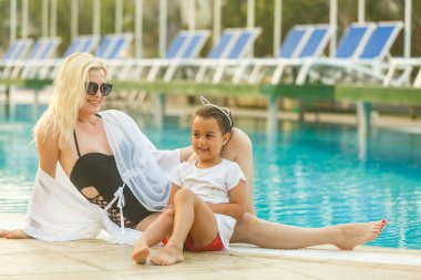 Yüzme havuzunun kenarında oturan kızı ile Genç Anne