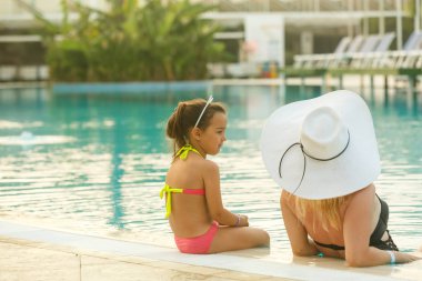 Yüzme havuzunun kenarında oturan kızı ile Genç Anne