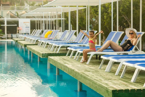 Yüzme havuzunun kenarında oturan kızı ile Genç Anne