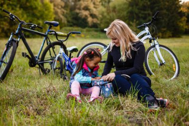 Genç mutlu anne ile küçük kız dinlenme içinde Park Near Bikes