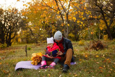 Mutlu baba ve kızı oturan ve sarı yaprakları üzerinde sonbahar parkta kitap okuma