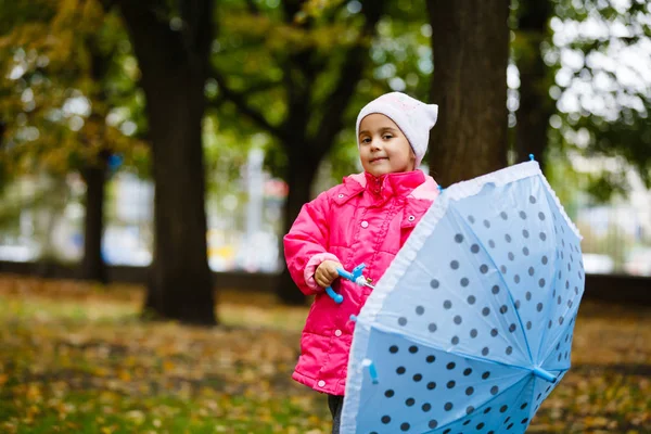 秋の公園で傘とピンクのレインコートで微笑む小さな女の子 — ストック写真