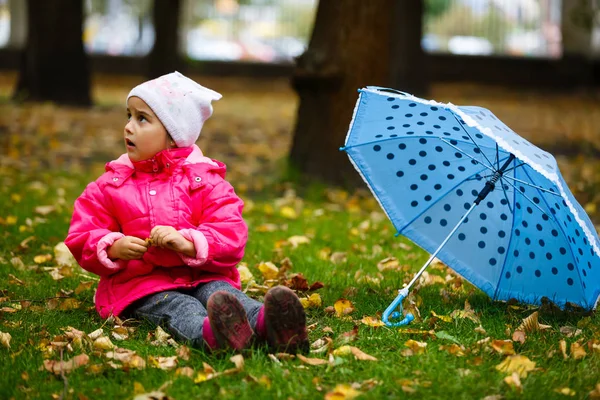 秋の公園で傘とピンクのレインコートで微笑む小さな女の子 — ストック写真