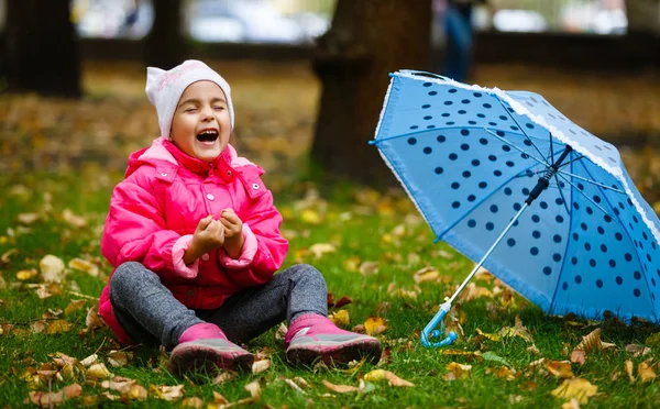 smiling little girl in pink raincoat with umbrella in autumn park